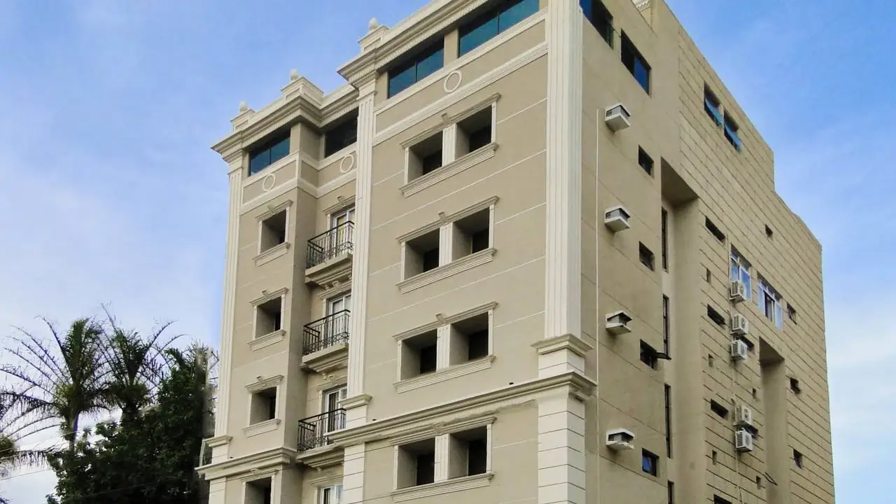 Fachada do Hotel Nações Plaza de dia: o prédio bege de seis andares, com palmeiras e o céu azul